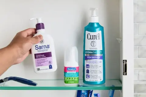 Dłoń sięga po balsam Sarna, by złagodzić swędzące plecy. Obok spray Benadryl i balsam Curél.