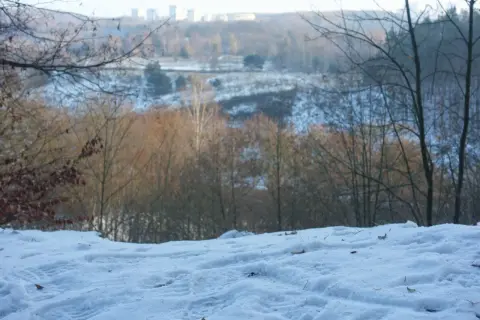 Śnieg pokrywa wzgórze, a w oddali widać zimowy krajobraz Gdańska z drzewami i budynkami.