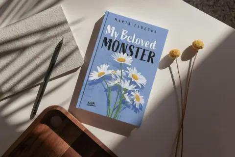Okładka książki "My Beloved MONSTER" Marty Łabeckiej, z motywem stokrotek. To piękna miłość książka dla dzieci, która zachwyci najmłodszych.