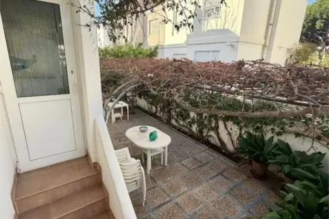 Patio con mesa y sillas bajo una pérgola cubierta de enredaderas secas. Un gran cortijo se vislumbra al fondo.