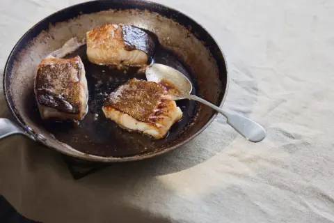 Stekt kolja i en panna, perfekt för ett enkelt kolja recept. En sked ligger bredvid fisken.