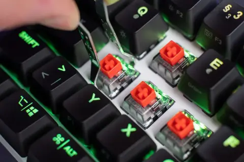 Nahaufnahme von Tastatur-Switches mit roten Kappen, die Unterschiede zeigen. Grüne Beleuchtung schimmert durch.