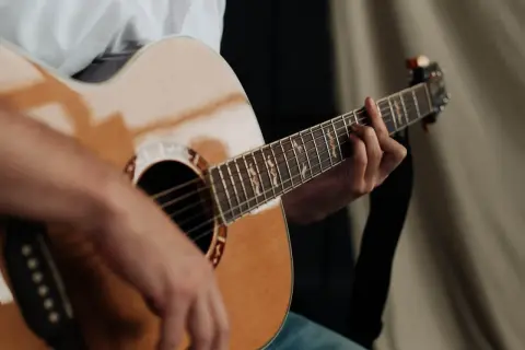 Dłoń grająca na gitarze akustycznej. Zastanawiasz się, ile trwa nauka gry na gitarze? To zależy od Ciebie!