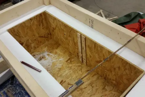Wooden frame with OSB interior, insulated with white foam. A pencil and ruler are visible.
