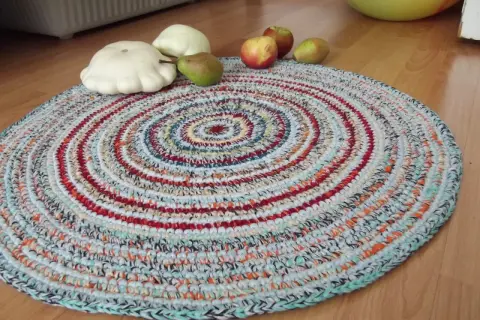 Tappeto uncinetto rotondo con fantasie a spirale multicolore. Sopra, zucche bianche, una pera e mele rosse.