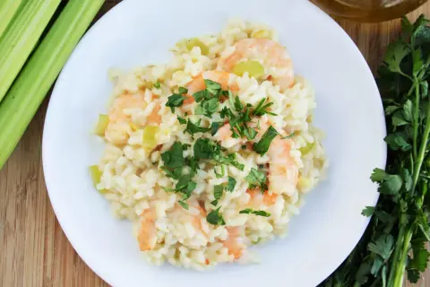 Pyszne risotto z krewetkami, udekorowane natką pietruszki, obok łodygi selera i oliwy.