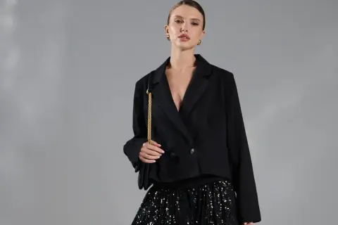 Modelka w czarnej marynarce i błyszczącej spódnicy z cekinami.