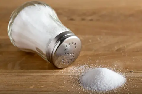 En saltkvarn ligger på ett träbord med en liten hög salt bredvid.