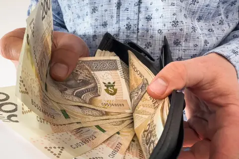Ręce trzymają portfel z banknotami 200 zł. Ile trzeba przepracować, by tyle zarobić?