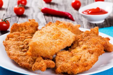 Chrupiące sznycle na białym talerzu, obok pomidorki i papryczka chili. Idealne na obiad!