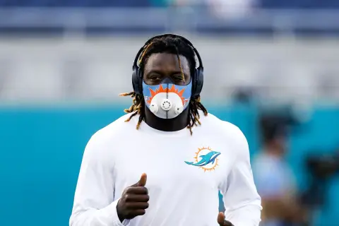 Miami Dolphins player running with an altitude mask training, headphones on, and giving a thumbs up.
