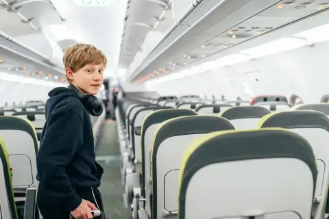 Chłopiec z słuchawkami na szyi w pustym samolocie. Zastanawia się, od ilu lat można latać samemu Ryanair.