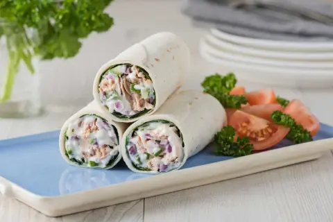Trois wraps au thon crémeux, garnis de thon, oignons rouges et concombre, servis avec des quartiers de tomates et du persil.