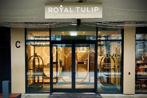 Eleganckie wejście do Royal Tulip Warsaw Apartments z widocznym logo i recepcją.