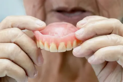 Manos de anciano sostienen una arcada dental superior, mostrando los dientes postizos.