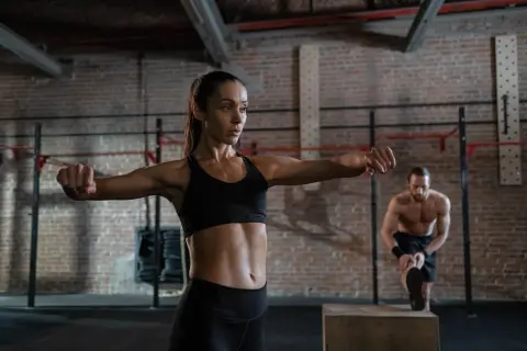 A woman performs boxing neck exercises in a gym. A man stretches in the background.