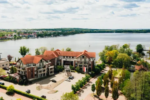Willa Port w Ostródzie, hotel z widokiem na jezioro, otoczony zielenią i zabudowaniami.
