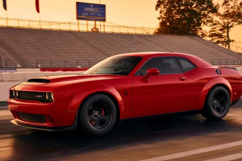 Czerwony Dodge Demon pędzi po torze wyścigowym podczas zachodu słońca, z trybunami w tle.