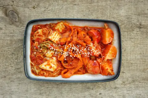 Gotowe kimchi z kapusty pekińskiej, z marchewką i sezamem, na drewnianym tle. Idealne do nauki jak zrobić kimchi z kapusty pekińskiej.