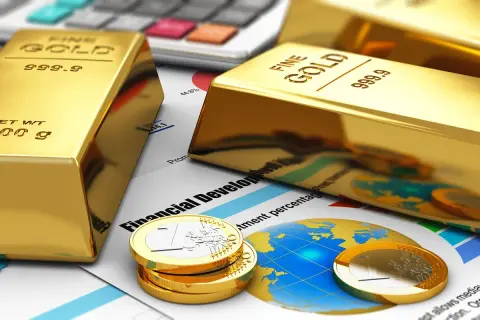 Sztabki złota i monety euro na tle wykresów i kalkulatora symbolizują inwestycję w złoto jako bezpieczną przystań finansową.