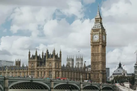 Big Ben i Parlament w Londynie, stolicy UK, na tle chmur. Most pełen ludzi i czerwony autobus.