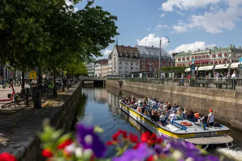 En paddanbåt med turister glider fram på kanalen i Göteborg. Blommor i förgrunden ger en färgklick.