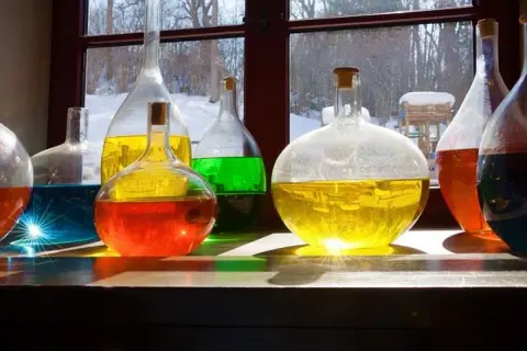 Kolorowe płyny w kolbach, jak uratować zoctowane wino? Słońce odbija się od szkła, tworząc magiczne refleksy.