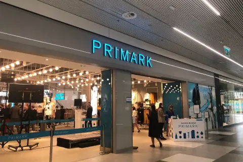 Wejście do sklepu Primark. W środku widać manekiny i ubrania. Na ladzie informacyjnej znajduje się **Primark tabela rozmiarów**.
