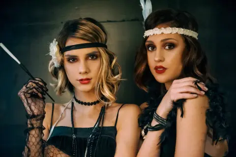 Dwie kobiety w stylu wielki gatsby stylizacja. Jedna z nich trzyma cygarniczkę, druga ma pióro we włosach.