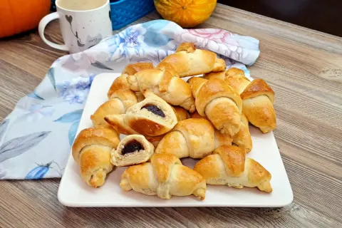 Pyszne rogaliki krucho drożdżowe z dżemem, ułożone na białym talerzu, obok kubka i jesiennych ozdób.