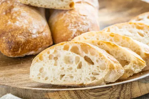 Frisch gebackene Ciabatta-Brote, aufgeschnitten auf einem Holzbrett. Das luftige Innere und die knusprige Kruste zeigen das gelungene Ciabatta Rezept.