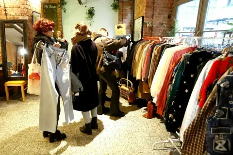 W sklepie z odzieżą vintage, gdzie króluje styl retro, kobiety przeglądają ubrania. To właśnie co oznacza słowo vintage – moda z minionych dekad.
