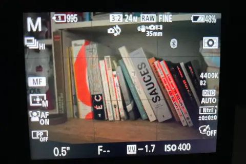 Livres sur une étagère, avec des lignes rouges indiquant le **focus peaking** sur les bords des livres. Réglages de l'appareil photo visibles.