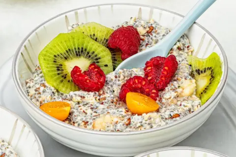 Schüssel mit Overnight Oats, garniert mit Kiwi, Himbeeren und Physalis. Ein Löffel liegt darin.