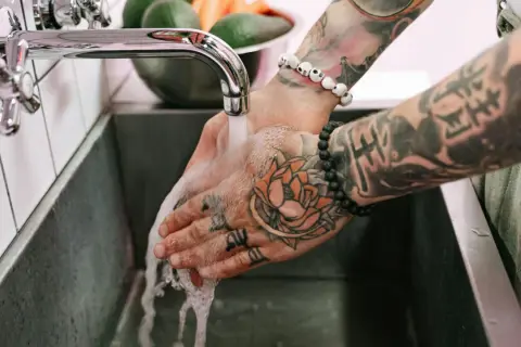 Hände mit Tattoos werden unter fließendem Wasser gewaschen, um die Pflege nach dem Duschen nach dem Tattoo zu gewährleisten.