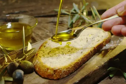 Olio d'oliva versato su pane, con olive e rametti d'ulivo. Un assaggio dei sapori autentici degli oleifici puglia.