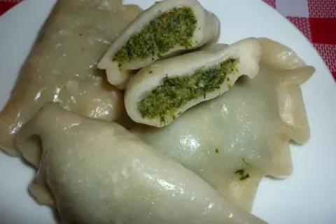 Pyszne pierogi ze szpinakiem i mozzarellą, jeden przekrojony, ukazujący zielone nadzienie.
