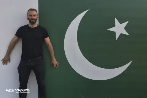 Mężczyzna w czarnym T-shircie i jeansach stoi obok flagi Pakistanu. Marzy o wizie do Pakistanu.