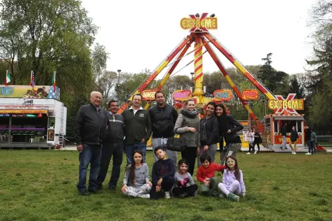 Famiglie giostrai italiani posano sorridenti davanti a un'attrazione "Extreme" in un parco divertimenti.