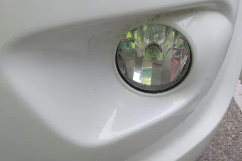 Zbliżenie na reflektor przeciwmgielny w białym zderzaku. Dowiedz się, jak włączyć światła przeciwmgielne, by poprawić widoczność.