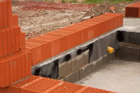 Budowa domu w toku. Widoczne pustaki ceramiczne o dużych wymiarach, fundamenty i rura odpływowa.