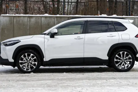 Biała Toyota Corolla Cross Hybrid na tle betonowego muru i śniegu. Stylowy SUV gotowy na zimowe wyzwania.
