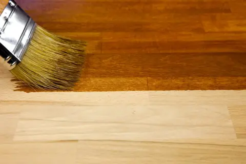 Un pinceau applique un vernis pour foncer du bois, transformant le bois clair en une teinte chaude et profonde.