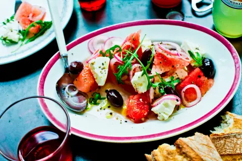 En läcker melon och fetaostsallad med oliver, rödlök och ruccola. Serveras med bröd och en kall dryck.