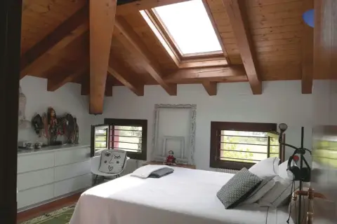 Camera da letto mansardata con travi a vista in legno. Idee colori per una mansarda luminosa e accogliente, con arredi bianchi e dettagli etnici.