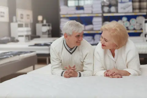Starsza para rozmawia, leżąc na białym materacu w sklepie.