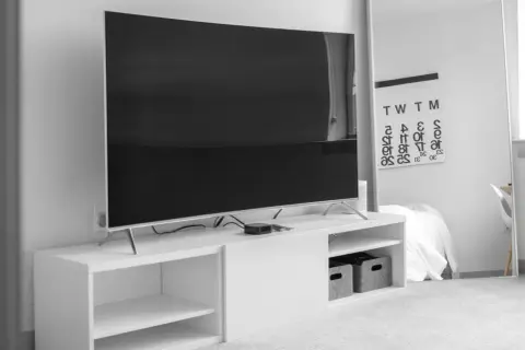 Nowoczesny salon z dużym telewizorem, którego wymiary to 75 cali, na białej szafce RTV. Obok lustro z kalendarzem.