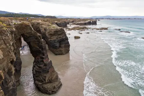Impresionantes arcos de roca natural en la playa de Ribadeo, con el mar Cantábrico rompiendo suavemente en la arena.