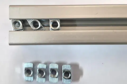 Kilka nakrętek wsuwanych do rowka teowego aluminiowego profilu.