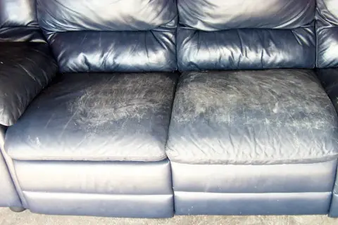 A dark blue leather couch with worn, scuffed seat cushions, showing the need for restoration.